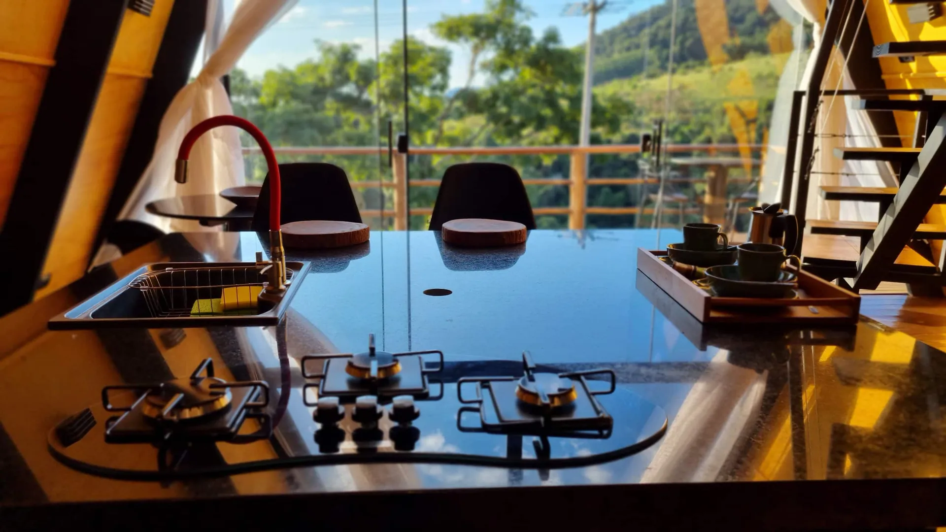 Ilha gourmet com cooktop, taças e vista pela porta de vidro