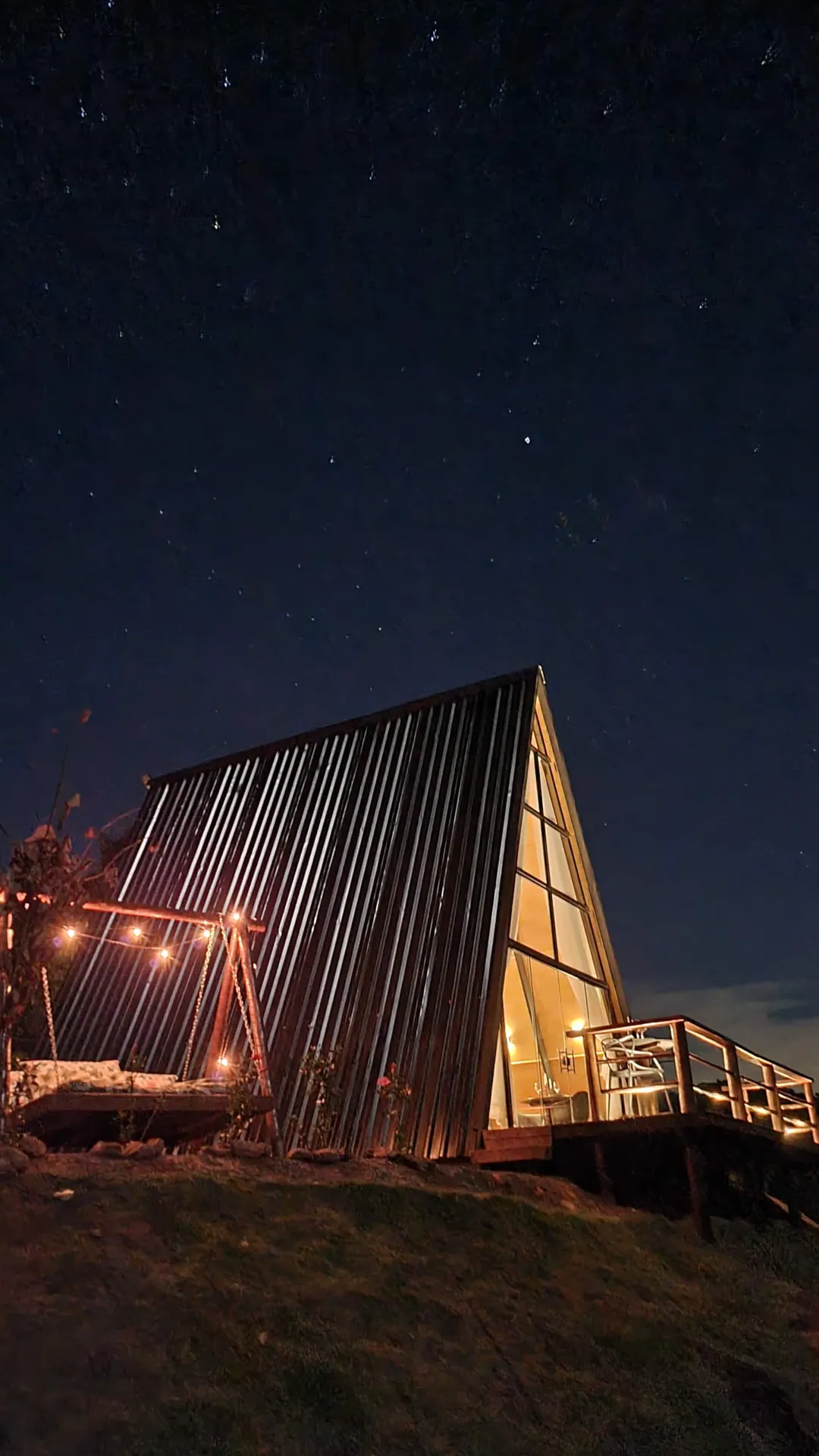O chalé iluminado à noite sob o céu estrelado, com a cama-balanço ao lado