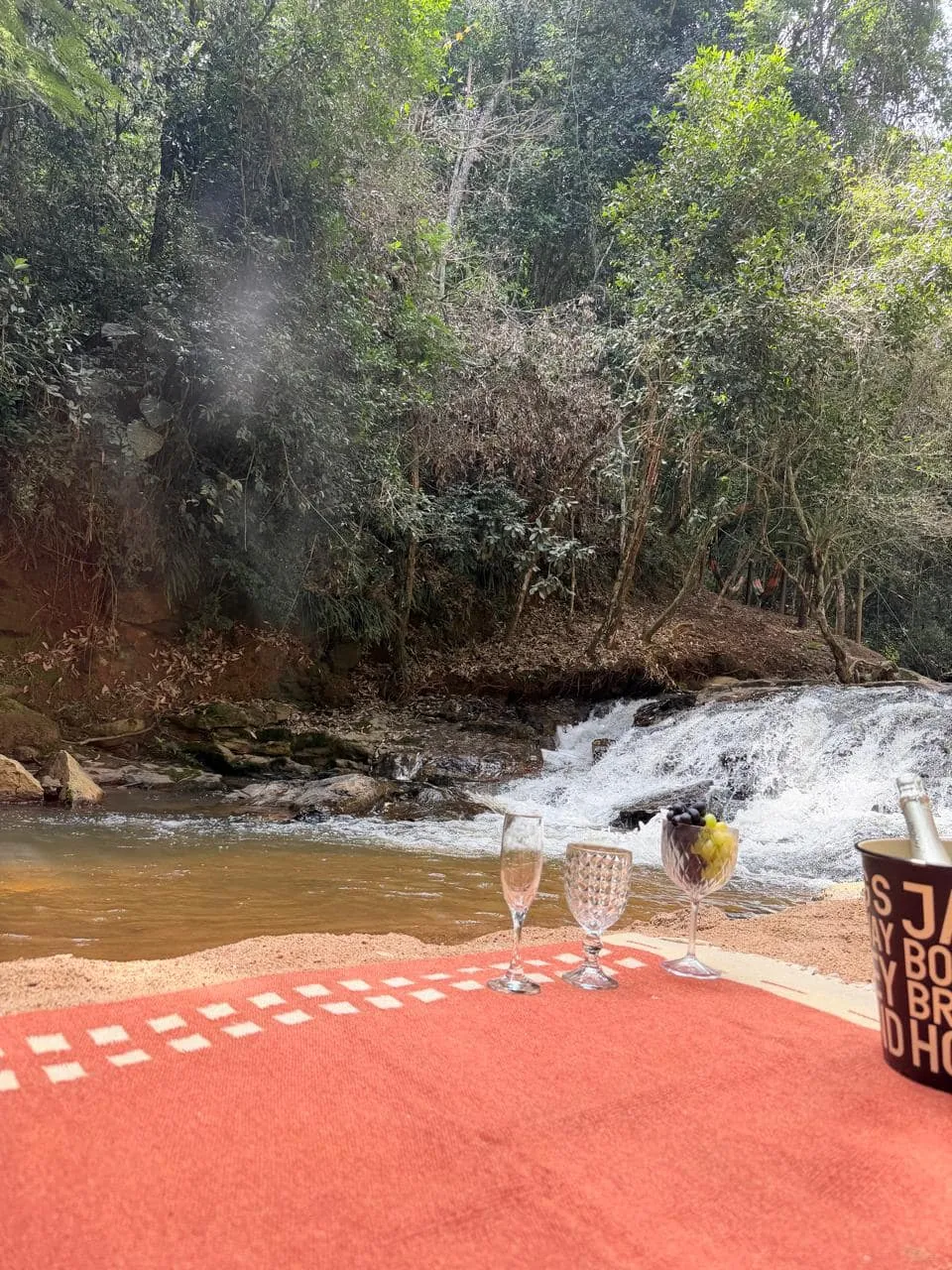 Toalha estendida à beira do rio, com taças e a queda d'água ao fundo