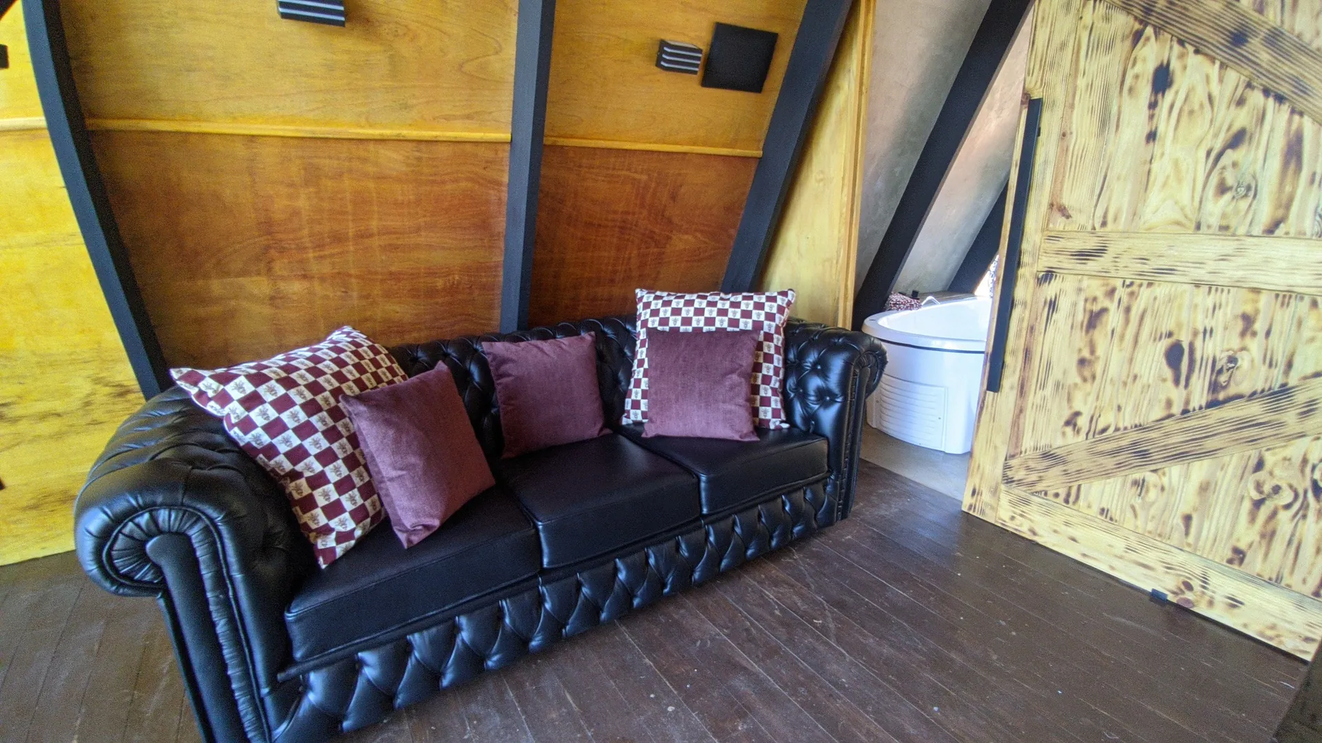 Sofá Chesterfield de couro com almofadas, sob a parede de madeira